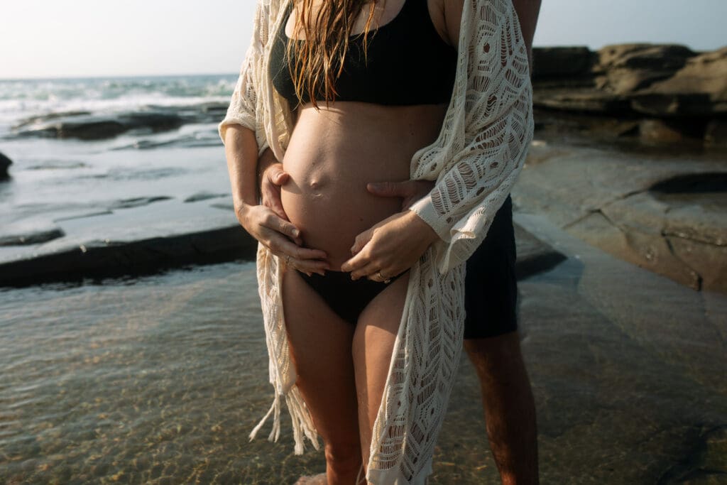 Pregnant couple holding the mums pregnant belly, the belly is gently lit by sunrise