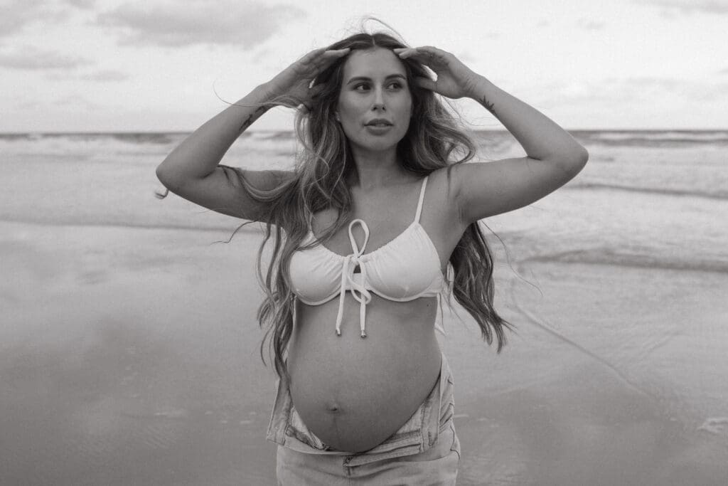Pregnant mum playing with her hair on burleigh beach , the sunset light gently lighting up her bare pregnant belly