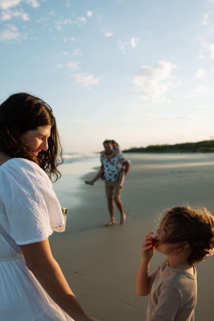 A family playing on the beach at Blackrock , Pottsville. The dad holding his older daugher in the background and mother holding the other daughters hands as they look at each other. The waves and beach are in the background and softly golden and deep blue shadows
