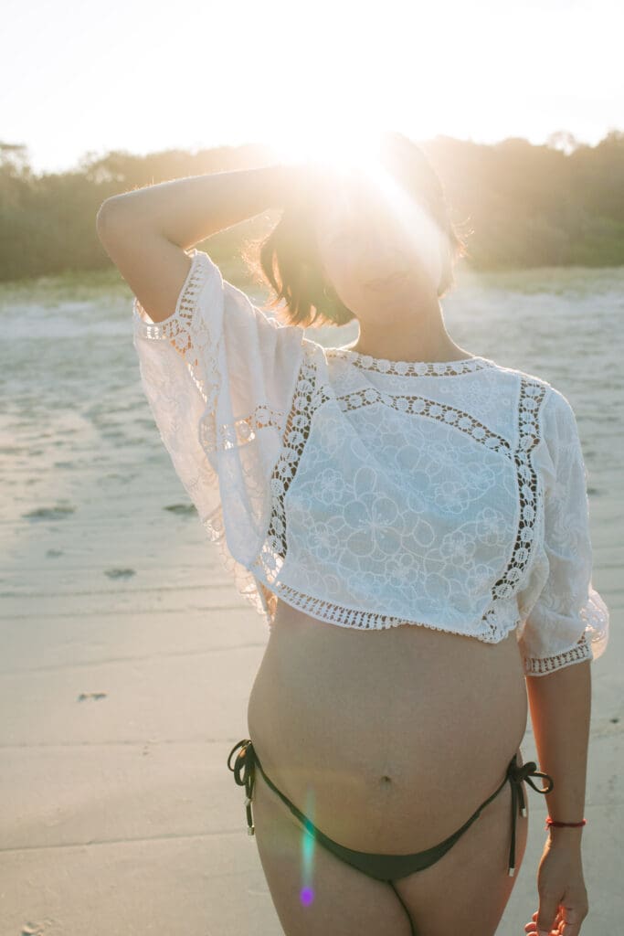 A pregnant mother stands in the twinkling setting sun at Broken head Beach near Byron Bay , the sand dunes are golden and glistening behind her