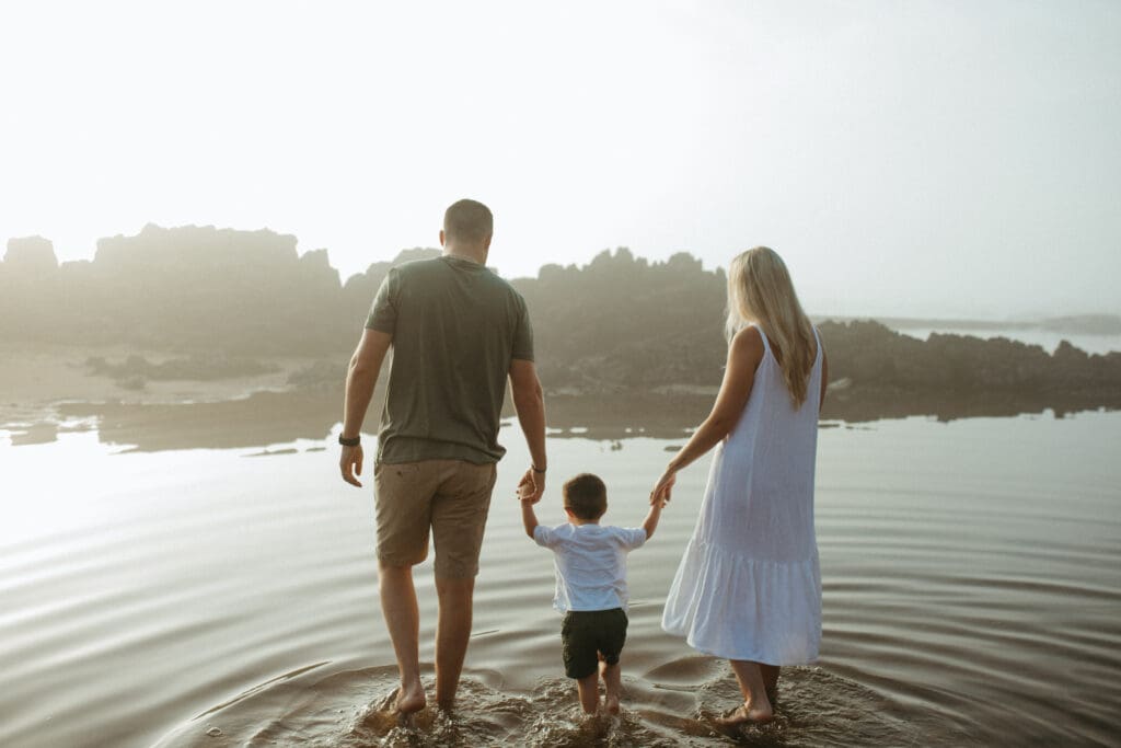 A family is in the water at a a beach in the Northern Rivers , Tweed Coast . They are holding hands and walking towards the Ocean. and being illuminated by the rising gold sun