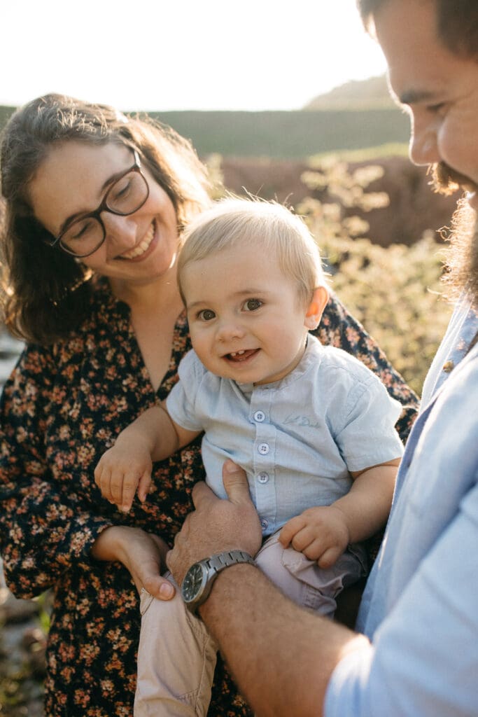 Mother ,father and happy gap toothed toddler boy all hugging tightly  in the sunset light at Pottsville. Grasses are glowing in the afternoon golden hour natural light