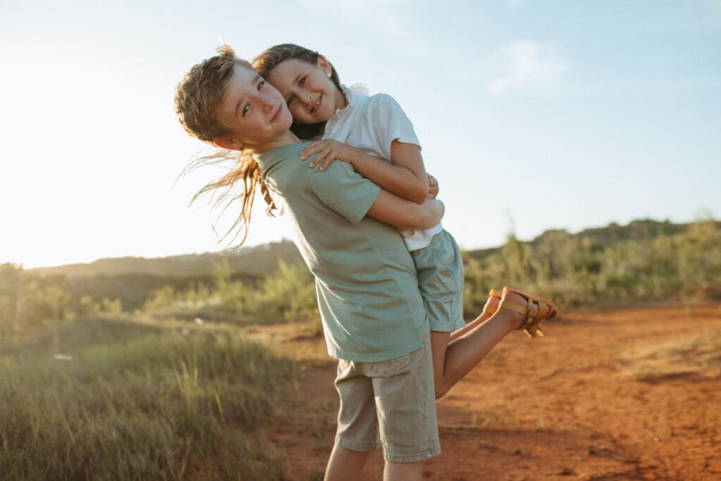 A brother and sister cuddling and laughing , the sun is setting on a dusty Murwillumbah farm road and the surrounding grass is golden 
