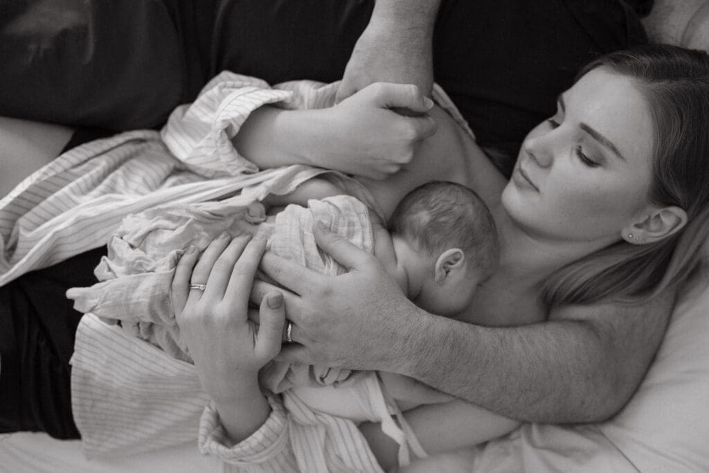 A mother and father  cradle their newborn son , their arms wrapped around the  sleeping baby