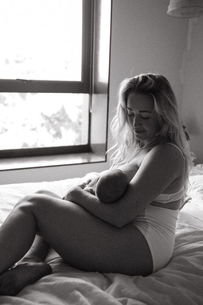 A mother feeds her baby by the window , it is an intimate moment as the mother gazes down and is lit by the window light