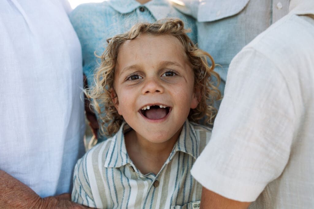Boy grins at at the camera , he is missing his front teeth and is framed my cousins in the soft light a t Pottsville creek