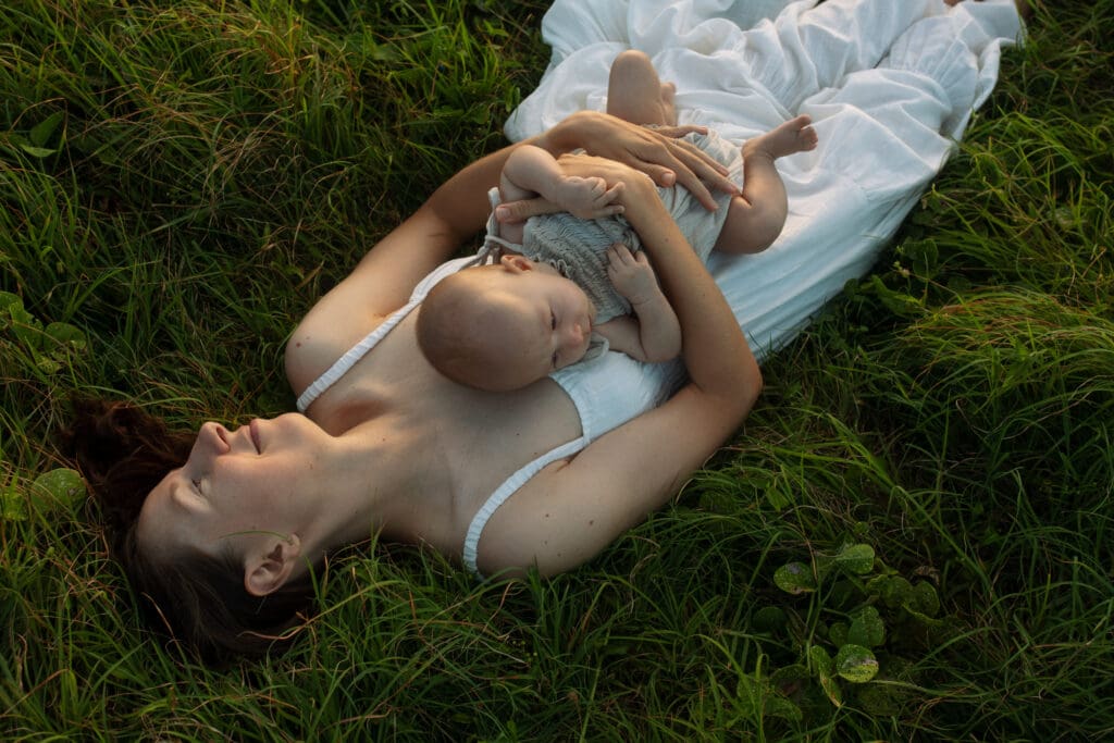 A mother lies in the grass at sunrise and holds her baby tightly and is glowing in the sunrise light at Lennox heads in the Northern Rivers