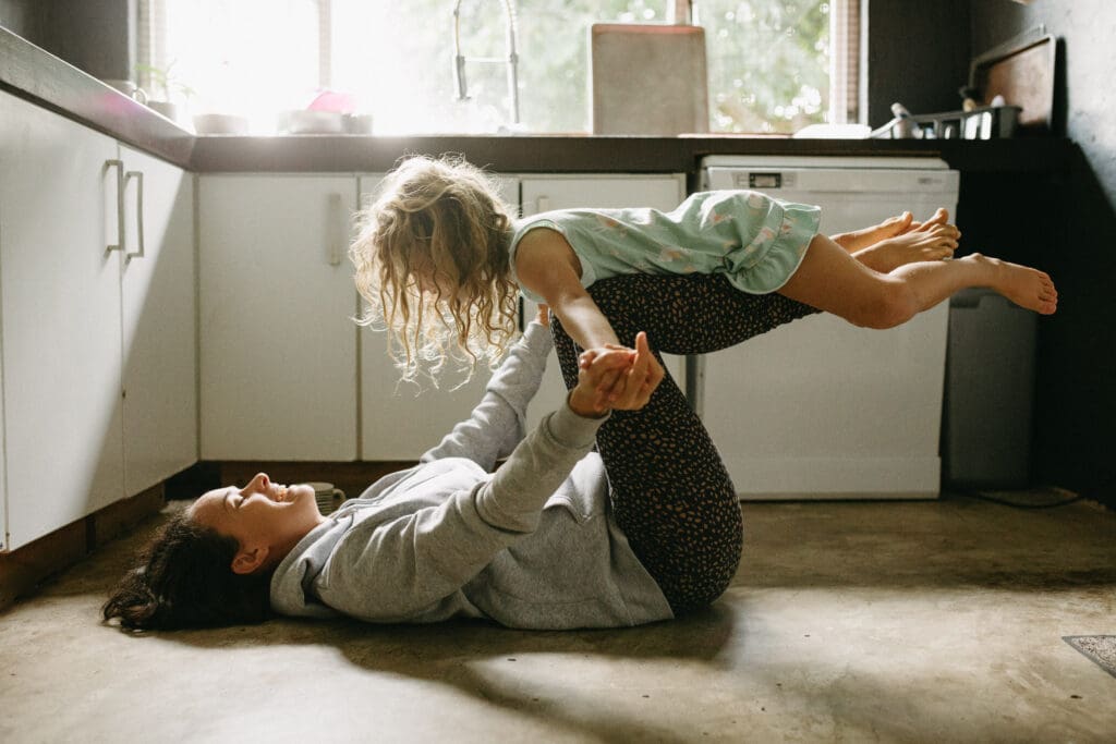 A mother plays with her giggling daughter in the kitchen and is lit up by the window light in their Pottsville home