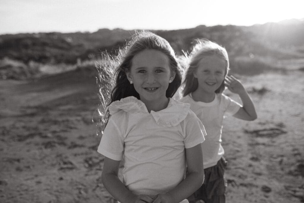 two cousins smile and giggle at the camera in golden sunset light. there is wind blowing their hair 
