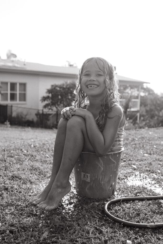 A girl is sitting in ha bucket in a pottsville back yard , she is grinning and missing teeth in a candid moment