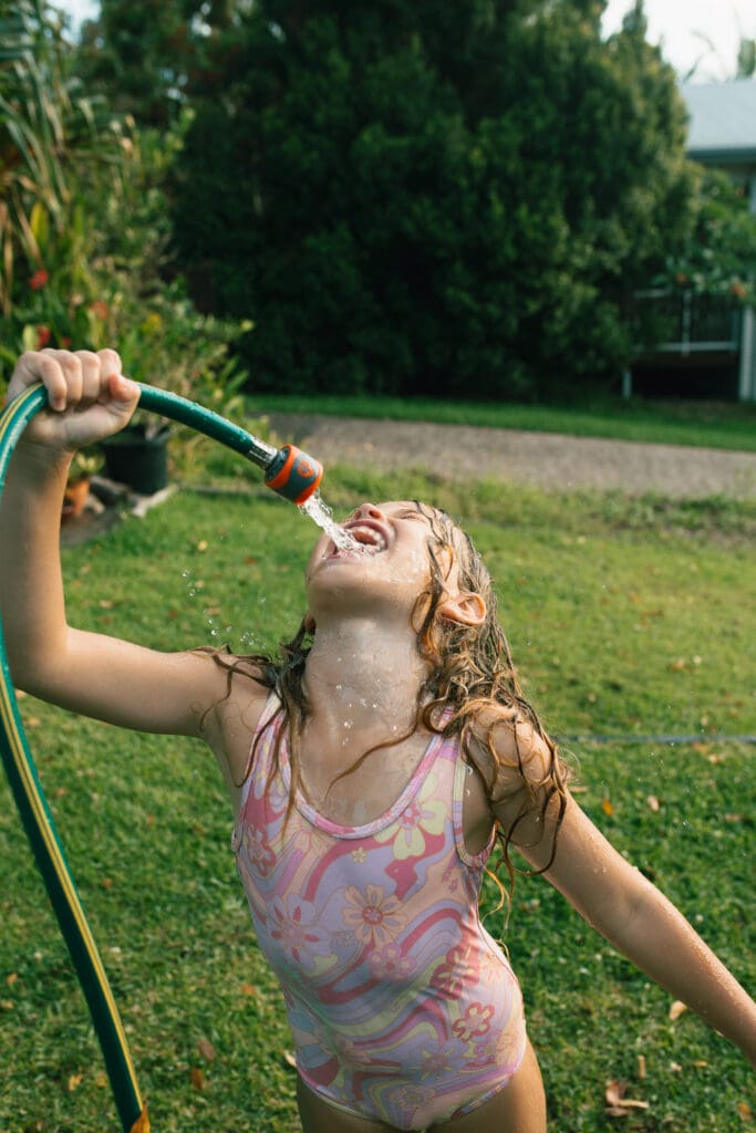 A girl drinks from the hosepipe in a Northern Rivers garden in Pottsville, she is joyful as the water splashes around her
