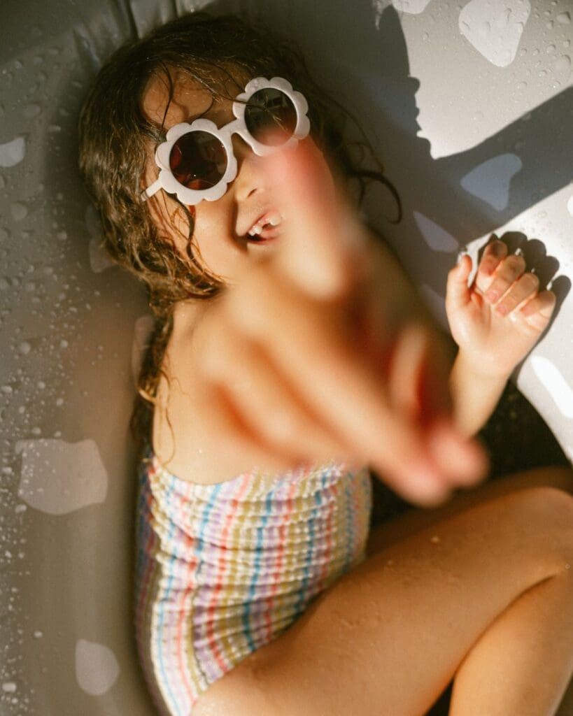 In a candid moment a girl is looking up and pointing at the camera , she is lying in a floaty and is missing teeth, is is playful and natural 