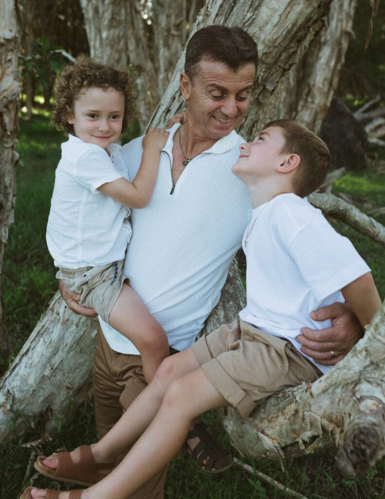 A grandfather jokes with his grandson who  is sitting in a paperbark tree  , the grandson stares adoringly at his Poppy.