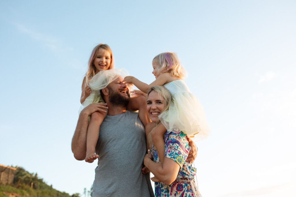 A family huddle in the morning light on a gold coast beach sunrise , the toddlers play with their laughing dad and the mom grins at the camera
