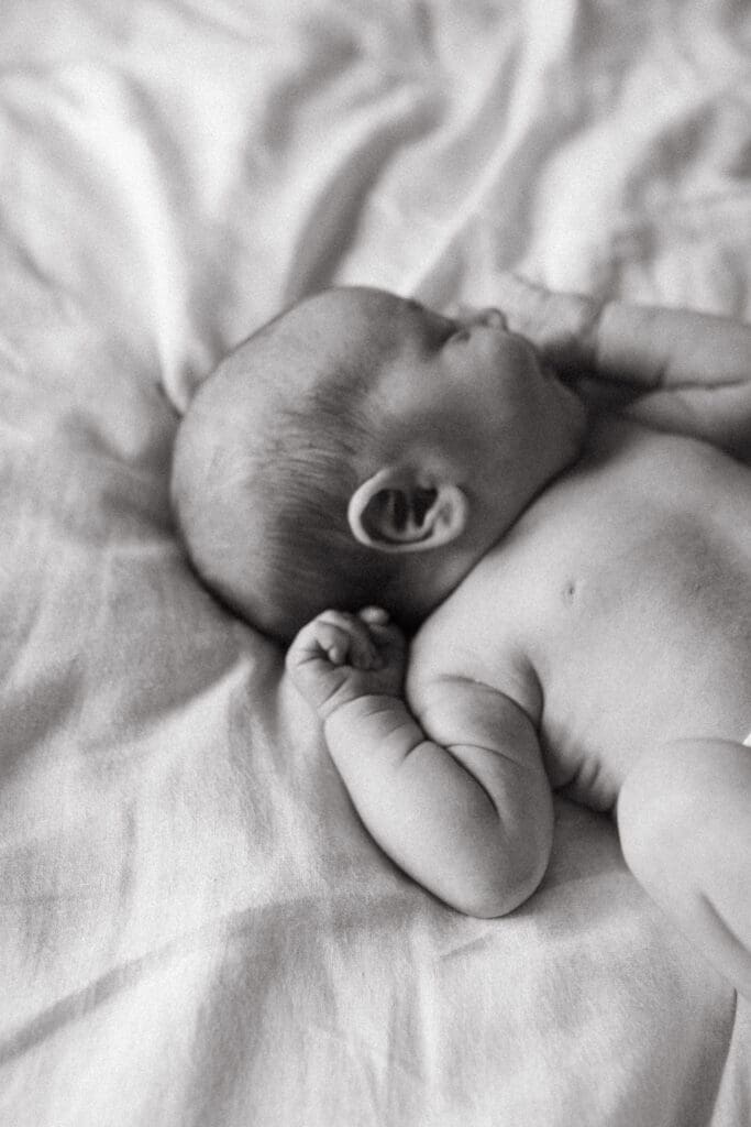 Newborn baby sleeping on a bed naturually lit , his arms and head in the light