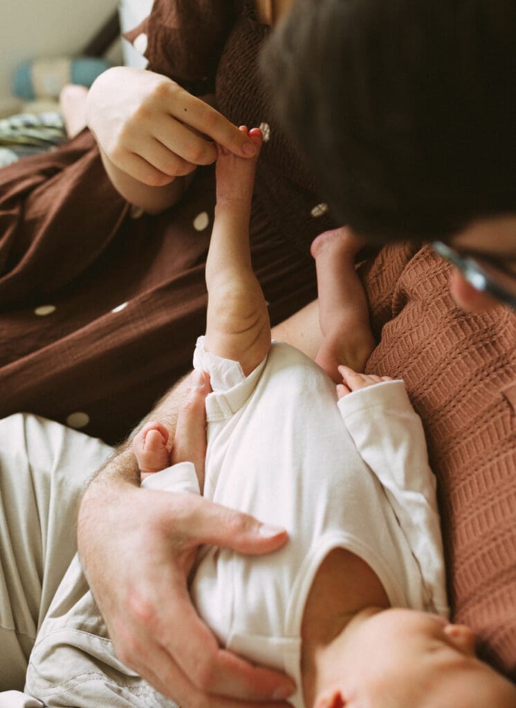 A sleeping newborn baby stretches out his legs ,while his mother plays with his little toes- a natural in home newborn photo