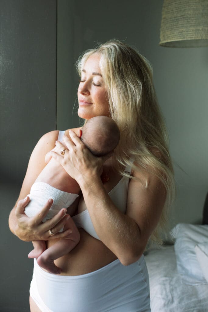 A new mother closes her eyes and cuddles her newborn baby boy in a minimal byron bay home