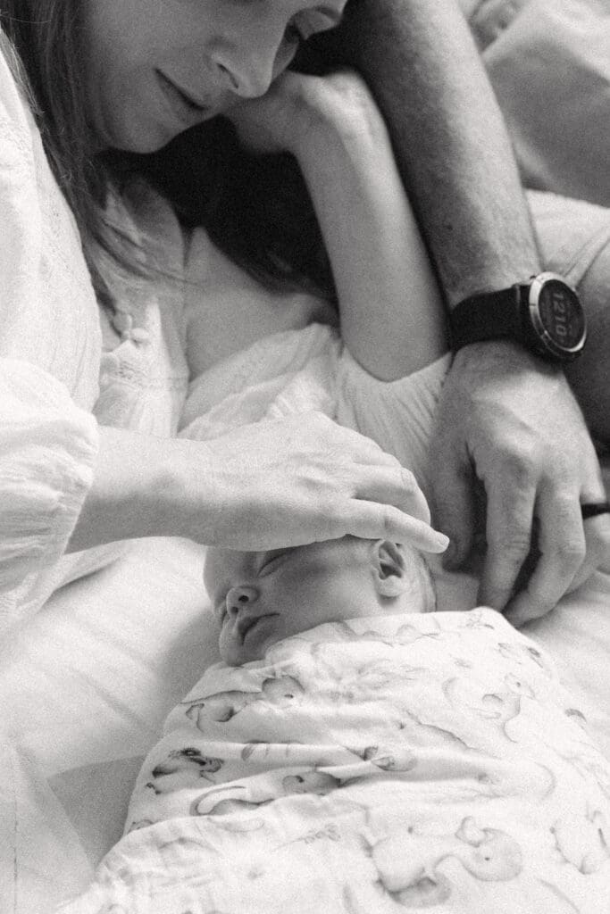 a mom and dad , new parents cuddle their newborn on their bed in their Gold Coast Home . Their baby is peacefully sleeping