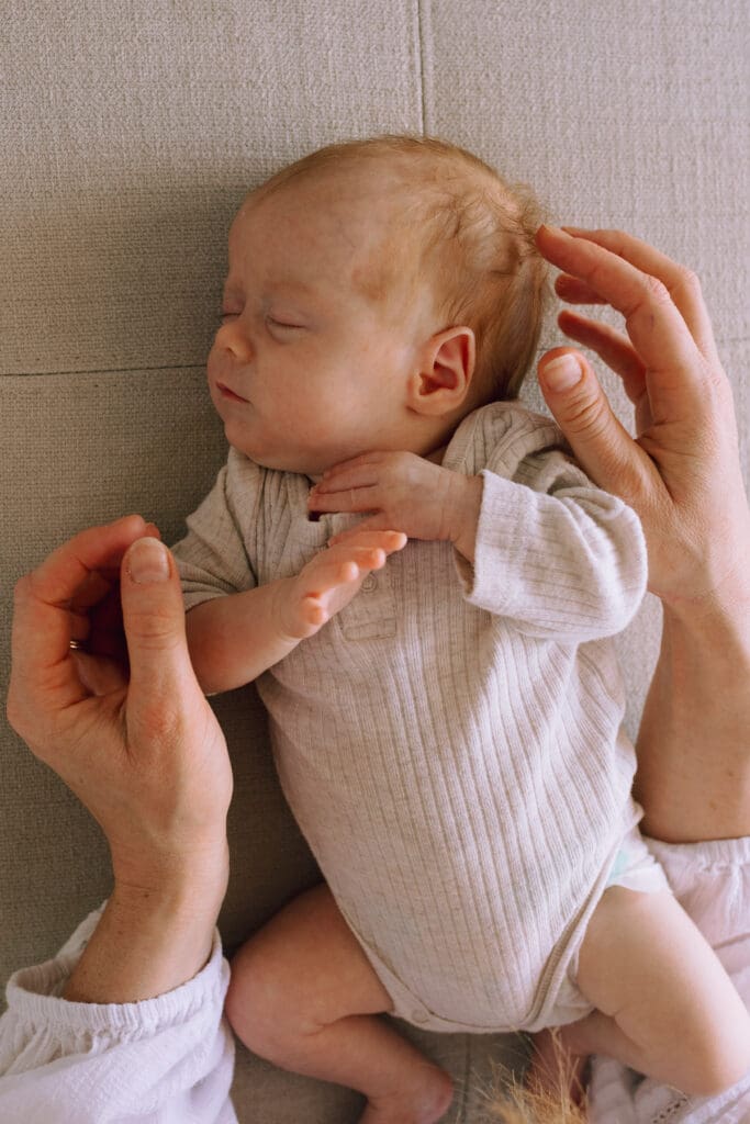 A mothers hands touch her babys hair while the baby sleeps