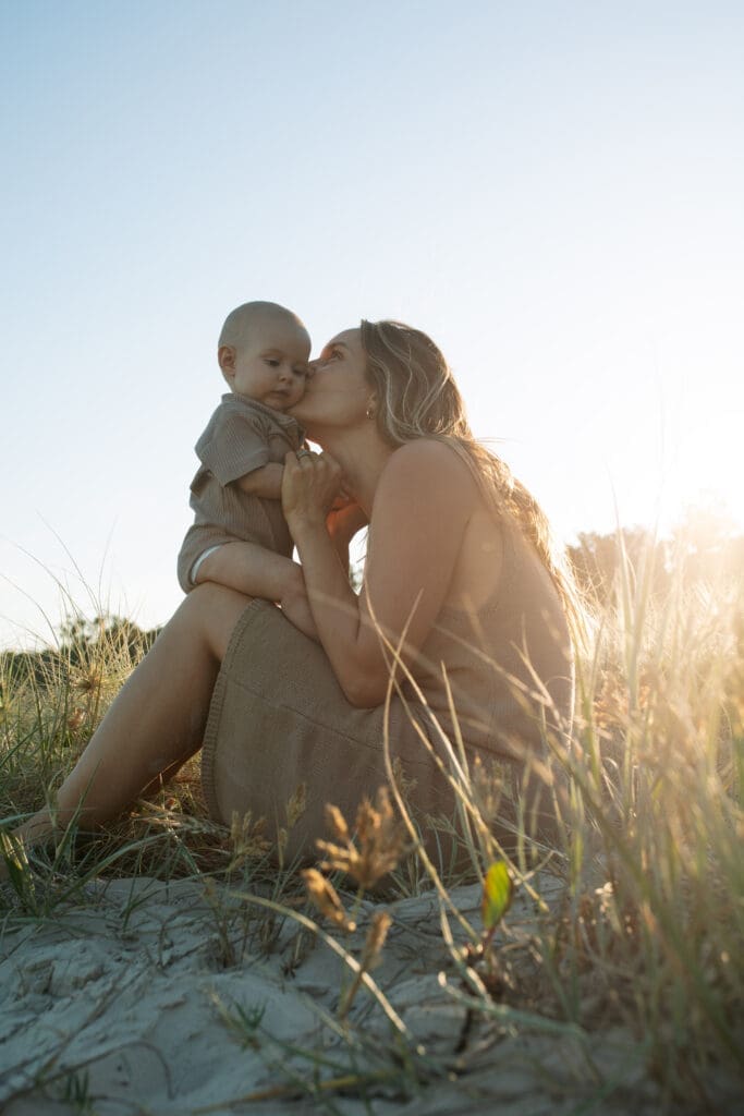 A mother kisses her baby in the grassy dunes at HAatings headland
