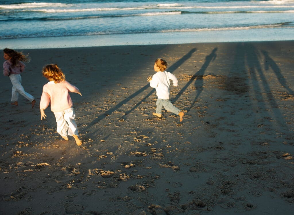 Children running along Cabarita Back Beach while their shadows stretch across the sand at sunset during an extended family session.