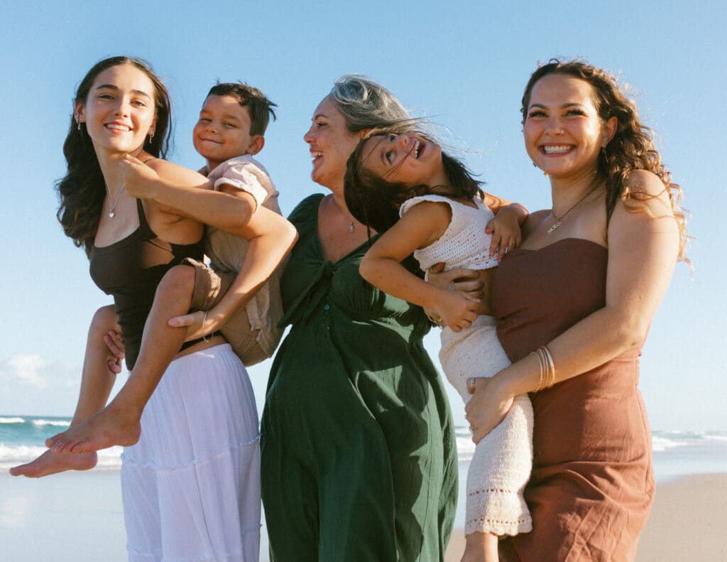 Multi-generational family laughing together on the beach in Kingscliff, kids being carried piggyback in candid documentary family photography