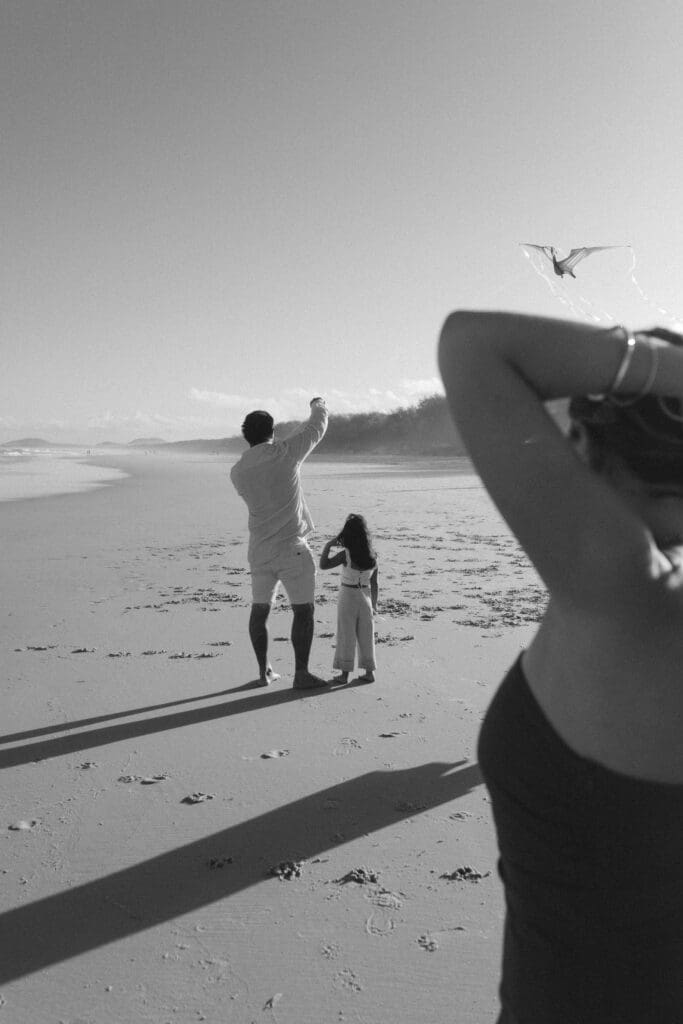 Black and white candid photo of a father and daughter flying a kite on the Tweed Coast during a family photoshoot