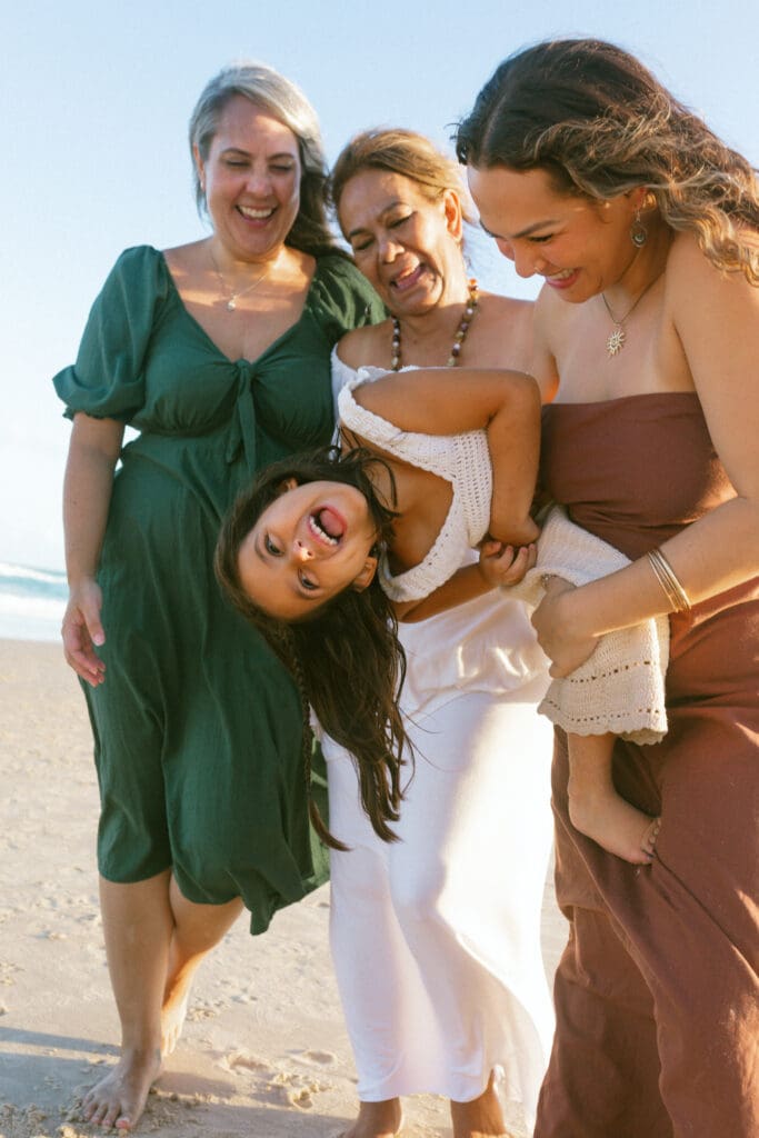 Grandmother, mother and toddler laughing together on Kingscliff beach during a candid family photography session
