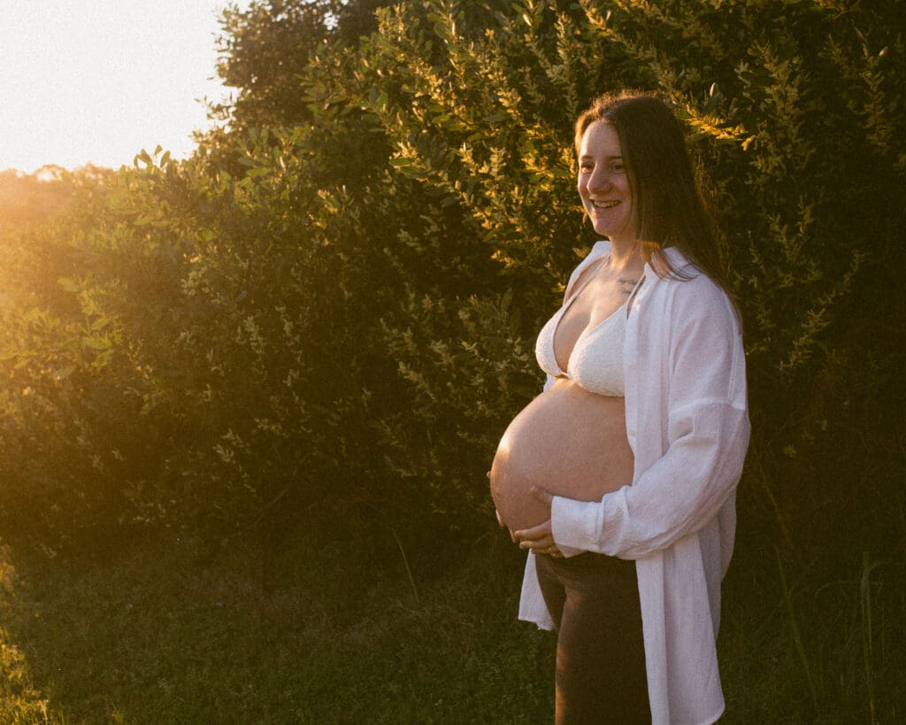 Pregnant woman holding her belly in warm golden light during her Byron Bay babymoon photoshoot