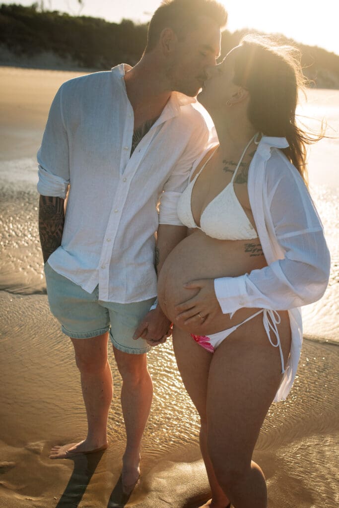 Expectant couple kissing in the golden afternoon light during their Byron Bay babymoon maternity photoshoot