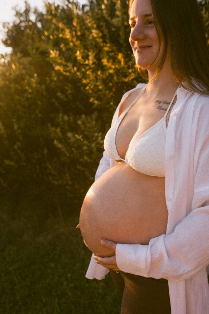 Pregnant woman holding her belly in warm golden light during her Byron Bay babymoon photoshoot