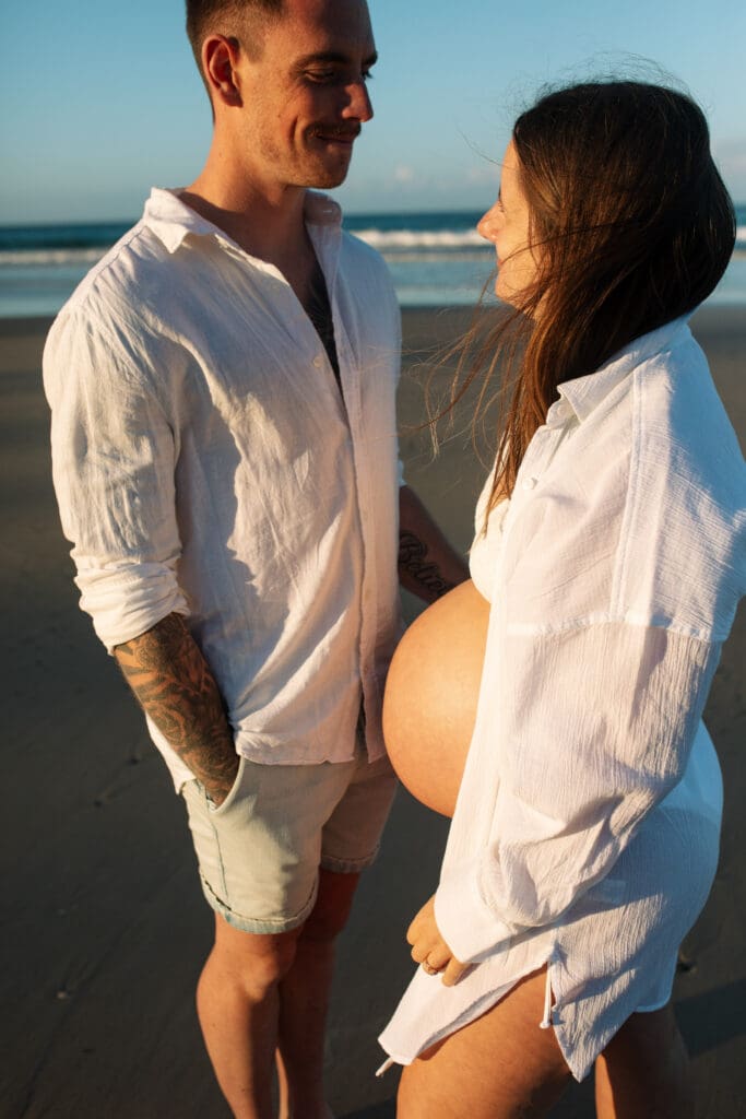 Expectant parents looking at each other during their maternity session at Belongil Beach near Byron Bay.
