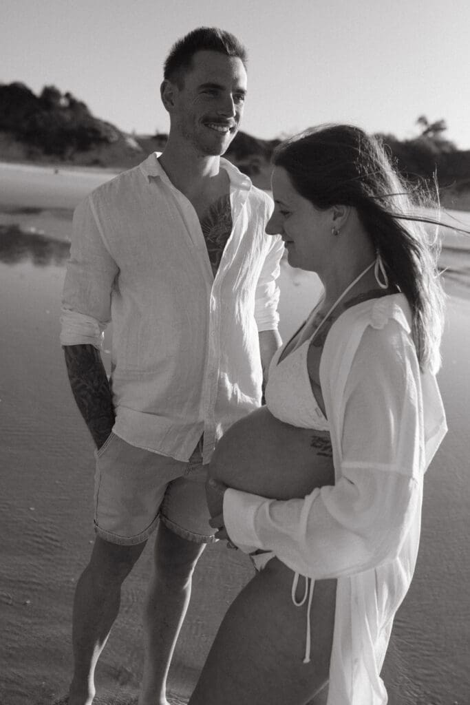 Black-and-white portrait of an expectant couple during their babymoon maternity session at Belongil Beach, Byron Ba