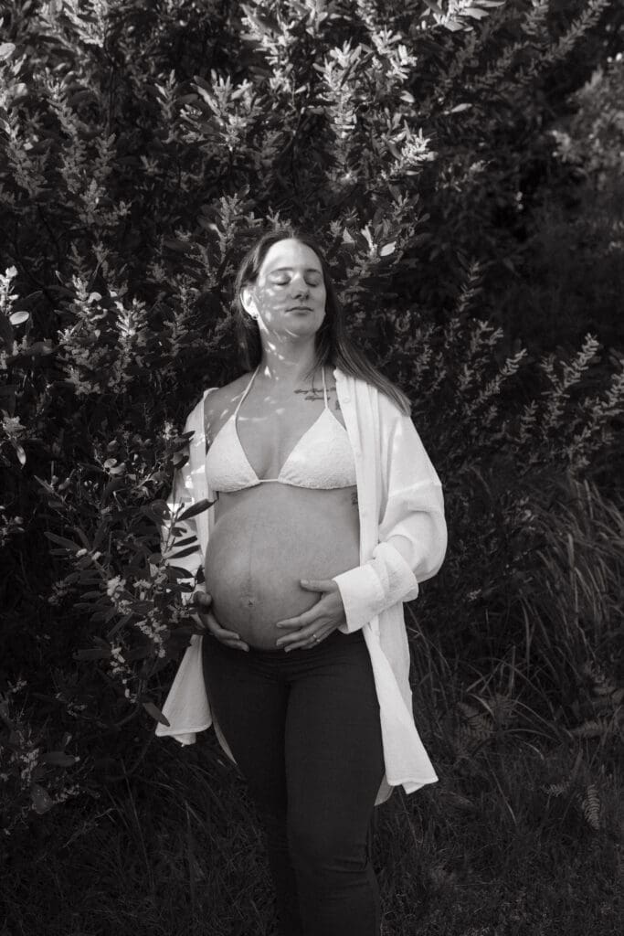 Black-and-white maternity portrait among the coastal greenery at Belongil Beach in Byron Bay.